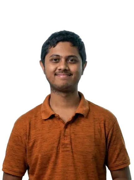 Portrait of a smiling man with short black hair wearing a brown-orange polo shirt, standing against a black background. Casual headshot with relaxed expression, centered composition, and soft studio lighting.